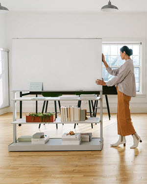 A woman pushes a moveable wall with shelves to create a temporary work room.